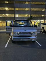 A silver Ford van, potentially an RV rental, is parked with both front doors open in a multi-level garage. Hawaii license plate.