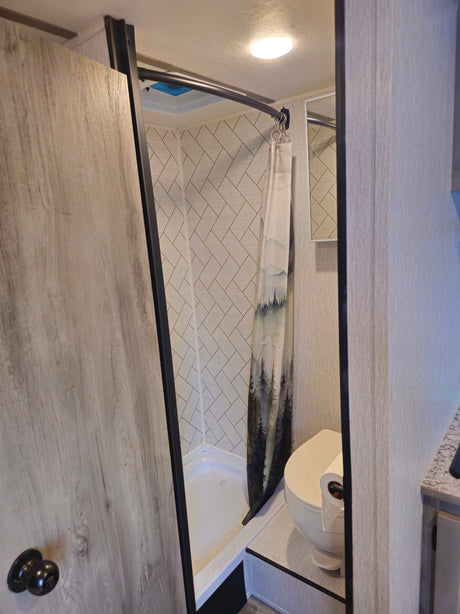 RV rental bathroom featuring a shower with a nature curtain, toilet, and wood-grain door. Includes tiled walls and mirror.