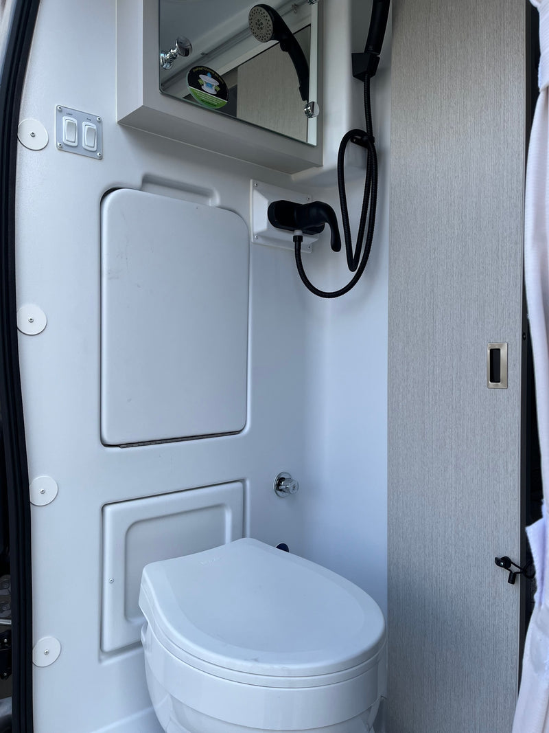 RV rental compact wet bath with a white toilet, shower, mirror, and light/fan controls on the wall. — photo 11