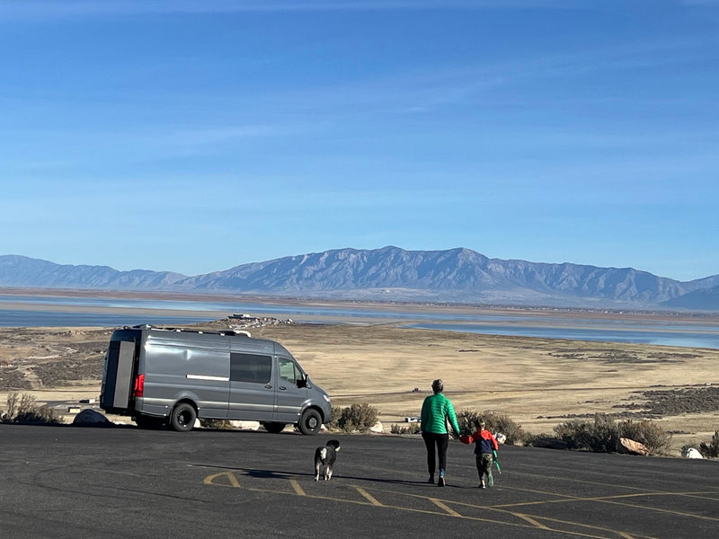 Enjoy an RV rental road trip! Family, dog, and a camper van by a scenic lake and mountains under a blue sky. — photo 5