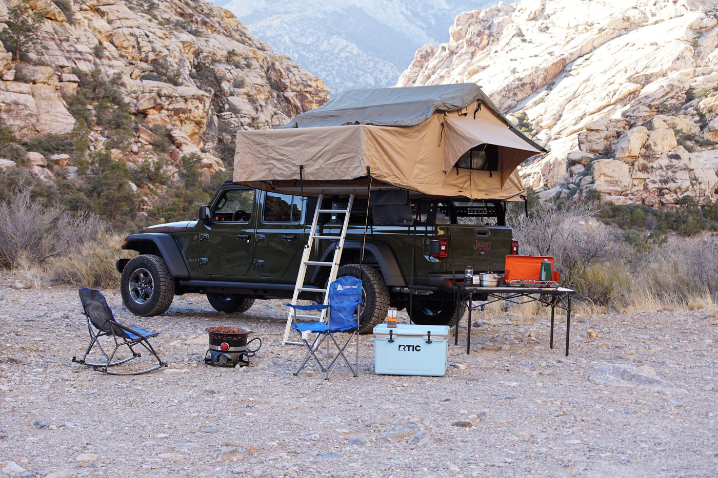 Experience off-grid camping with an RV rental! Jeep Gladiator, rooftop tent, cooler, chairs, and stove in a desert landscape. — photo 5