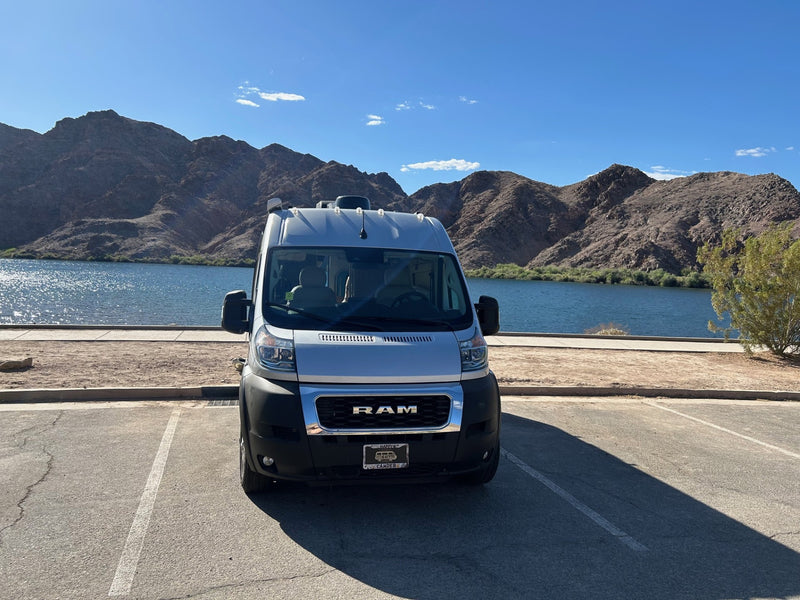  & people under a blue canopy in the background.|Silver RV rental van parked by a scenic lake with mountains — photo 9
