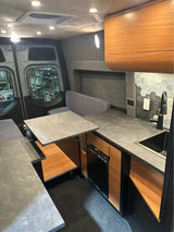 Sleek camper van interior for RV rental: modern compact kitchen with sink/fridge, plus a versatile dining area. Ideal for travel.