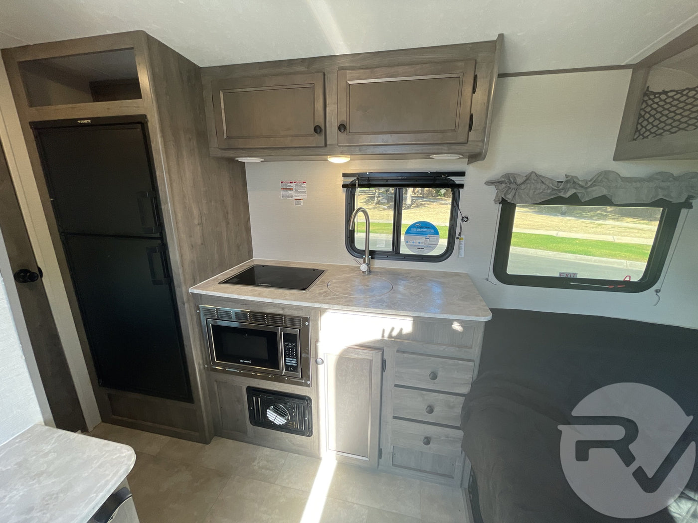 Explore this RV rental's interior, showcasing a compact kitchen with stove, microwave, sink, fridge, and sleeping area. — photo 8