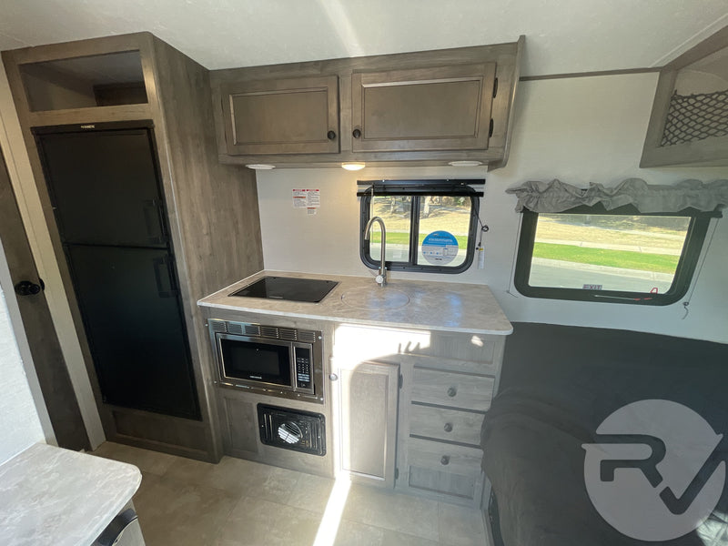 Explore this RV rental's interior, showcasing a compact kitchen with stove, microwave, sink, fridge, and sleeping area. — photo 8