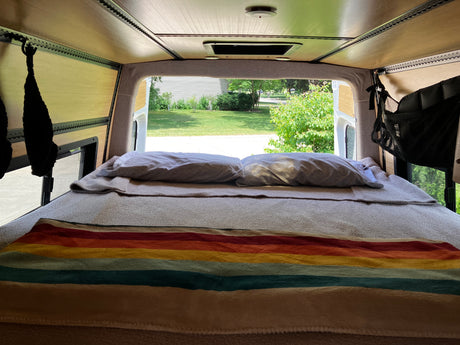 RV rental's cozy interior: wood-paneled walls, bed with colorful blanket, peaceful suburban view out back.