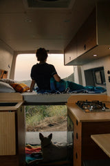 Cozy rv rental: A person on the bed and a dog below enjoy the sunset view from their camper van.