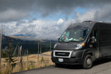 Dark grey RV rental van, a Ram ProMaster, parked on a scenic mountain road with cloudy skies and forest views.