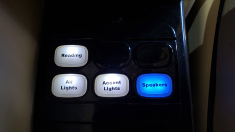 RV rental interior control panel with illuminated buttons: Reading, All Lights, Accent Lights (white), and Speakers (blue).