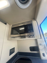 RV rental interior: A modern galley features a stainless microwave, dark countertop with a sink, and light walls.