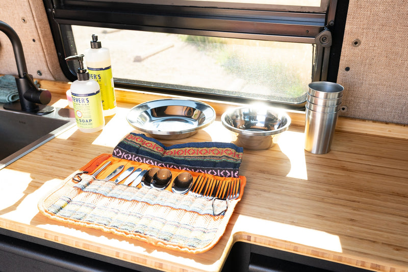 RV rental camping kitchen setup with dishes, soap, and cutlery on a wooden counter by a sunny window. — photo 10
