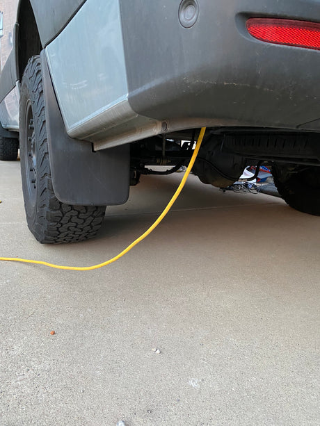 RV rental: A yellow power cable runs from the van's rear undercarriage to the concrete ground by the tire.