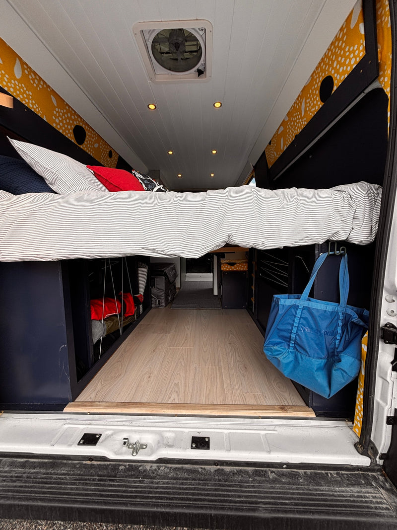 Cozy rv rental camper van interior: elevated bed, under-bed storage, wood floor, white ceiling with fan & lights. Ready for travel! — photo 15