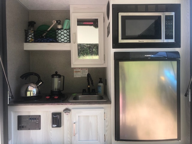 Well-equipped RV rental kitchen: microwave, Dometic fridge, two-burner stove, sink, and cooking essentials.