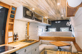 This custom RV rental interior features a functional kitchen, cozy dinette, and a raised bed. Ideal for van life travel.