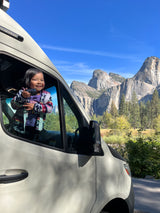 Joyful child in RV rental, admiring stunning Yosemite mountains and waterfall view from van window.