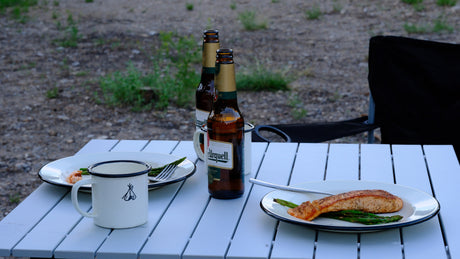 A camping table with plates of salmon, shrimp, asparagus, and beer bottles. Ideal outdoor dining for your next RV rental trip.