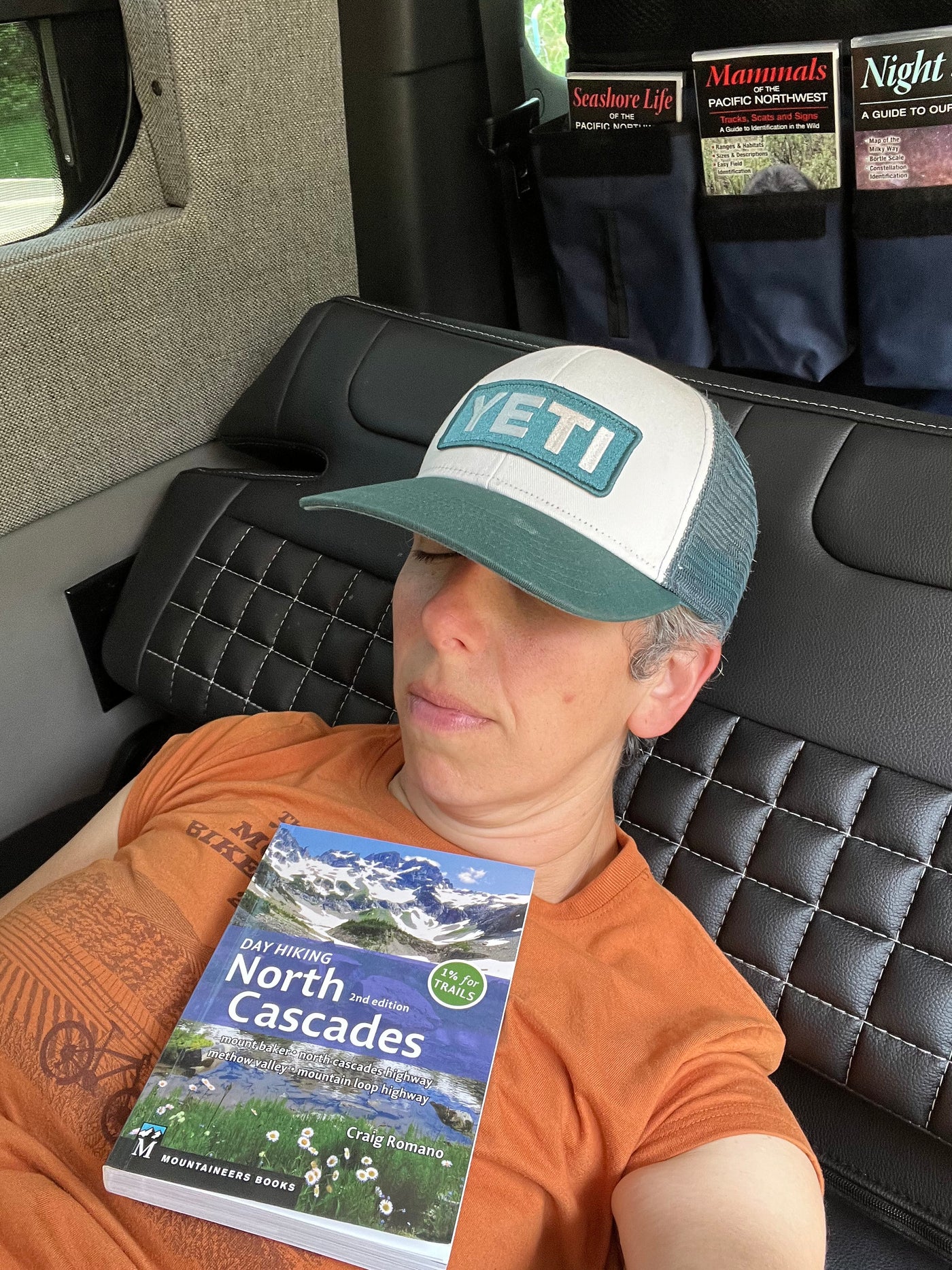 An adventurer naps in an RV rental, with a "Day Hiking North Cascades" book on their chest & nature guides nearby. — photo 15