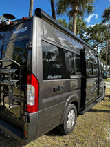 Dark grey Winnebago Travato rv rental. This camper van features an awning and rear rack, ideal for road trips.