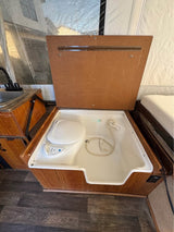 RV rental pop-up camper's compact bathroom: open wooden lid shows a toilet, shower, and sink.