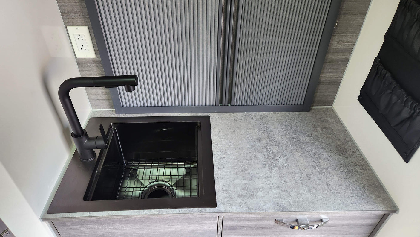 Modern RV rental kitchen featuring a sleek black sink, light gray counter, and convenient storage solutions.