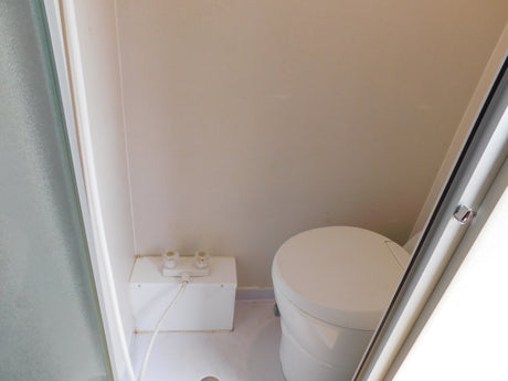 RV rental bathroom with compact shower area (controls & hose) and a round, self-contained toilet.