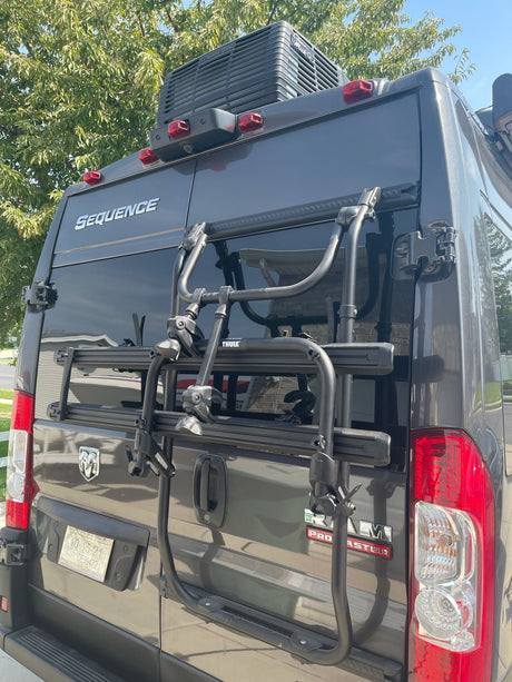 Rear of a grey Sequence RV rental (Ram ProMaster) shows a Thule bike rack. Perfect for outdoor adventures.
