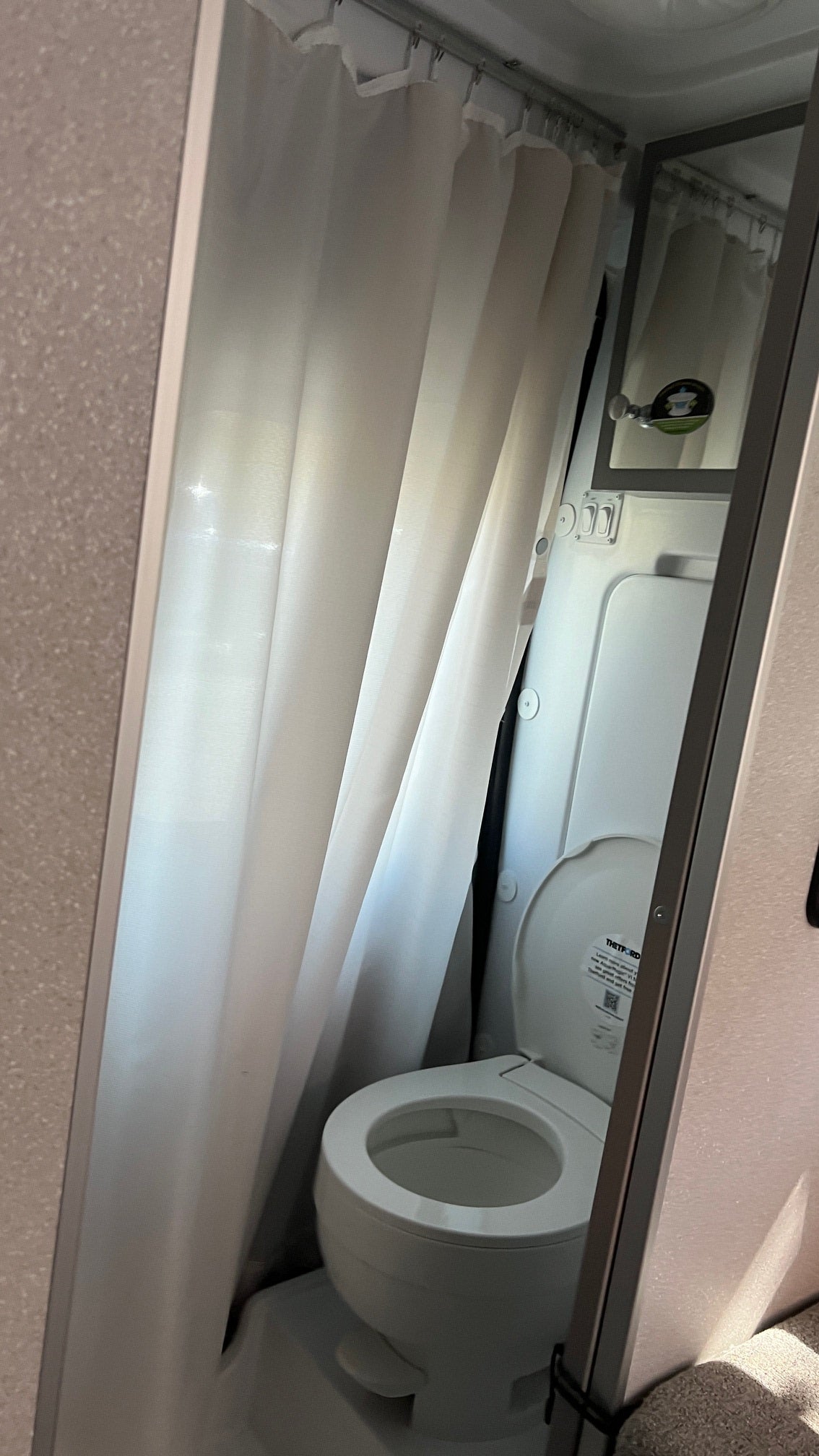 Inside an RV rental, a compact bathroom shows a white toilet with the lid open and a white shower curtain to the left.