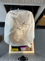 Inside an RV rental: White trash bag ready for use, with cleaning supplies like Campsuds and a sponge in lower storage.