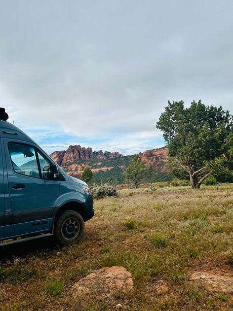 Experience freedom with an rv rental! Blue camper van overlooks a vast field & stunning red rock