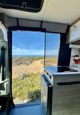 Stunning ocean view from an RV rental. This camper van offers a beachside cooking area & open door to coastal beauty.