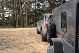 A tan SUV and gray overland trailer, ideal for an RV rental adventure, parked on a dirt road by pine and aspen trees.