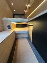 Step inside this cozy RV rental's wooden interior, featuring bunk beds, a control panel, and ambient lighting.