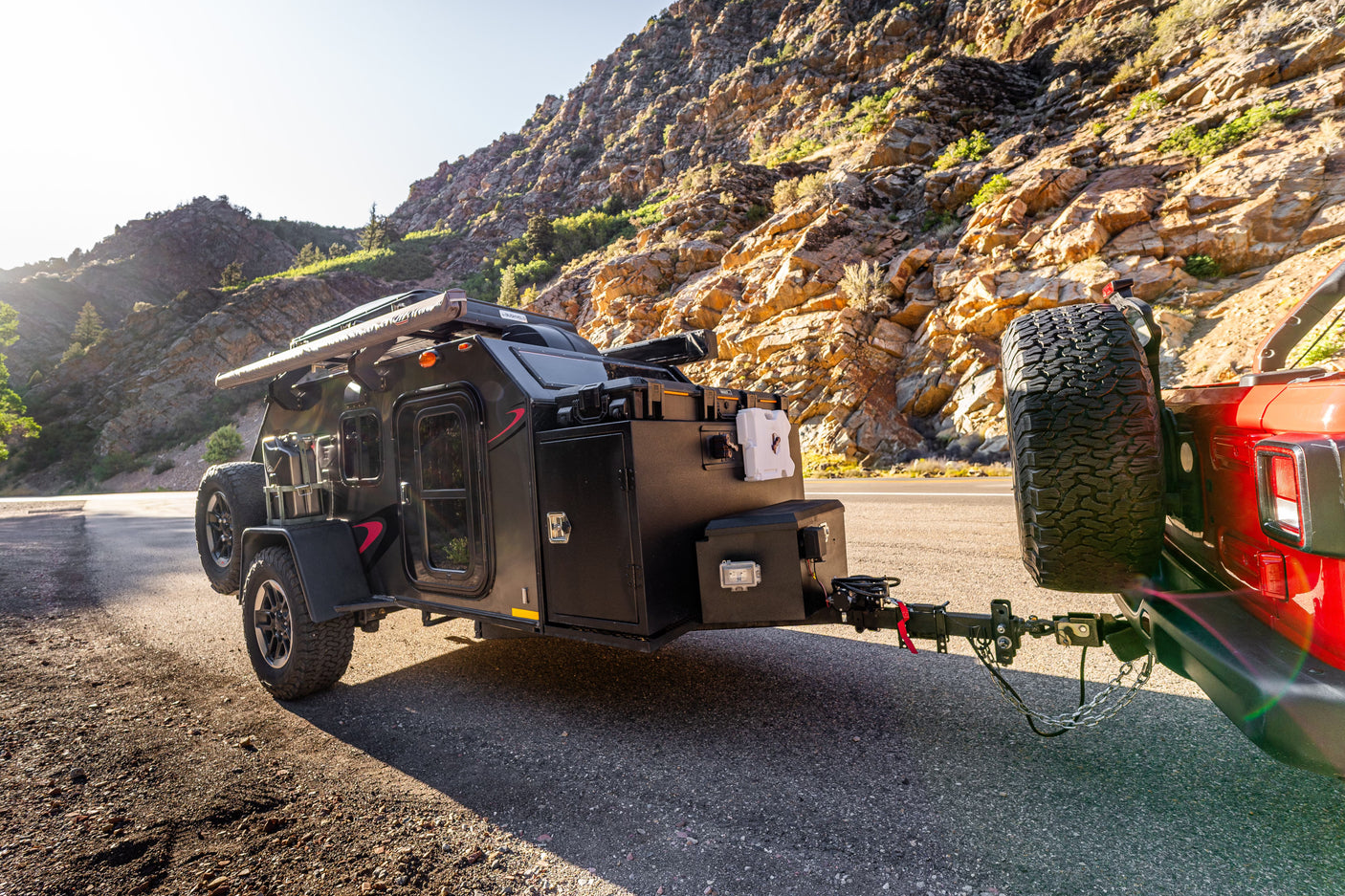 **RV rental**: A rugged black off-road trailer hitched to a red Jeep stands on a mountain road, ready for adventure.