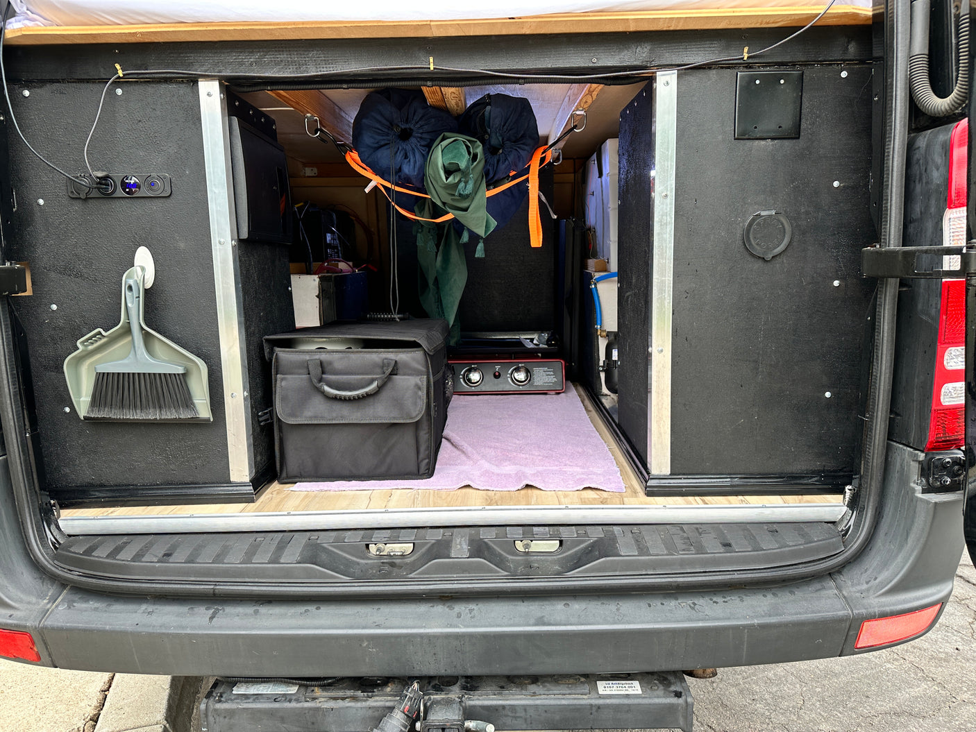 Inside an RV rental, the rear hatch reveals organized camper van storage, a portable stove, and power outlets for mobile living.