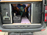 Inside an RV rental, the rear hatch reveals organized camper van storage, a portable stove, and power outlets for mobile living.