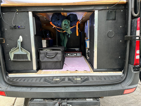 Inside an RV rental, the rear hatch reveals organized camper van storage, a portable stove, and power outlets for mobile living.