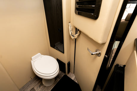 Compact RV rental bathroom: a white toilet against cream walls, dark wood accents, and laminate flooring for travel comfort.
