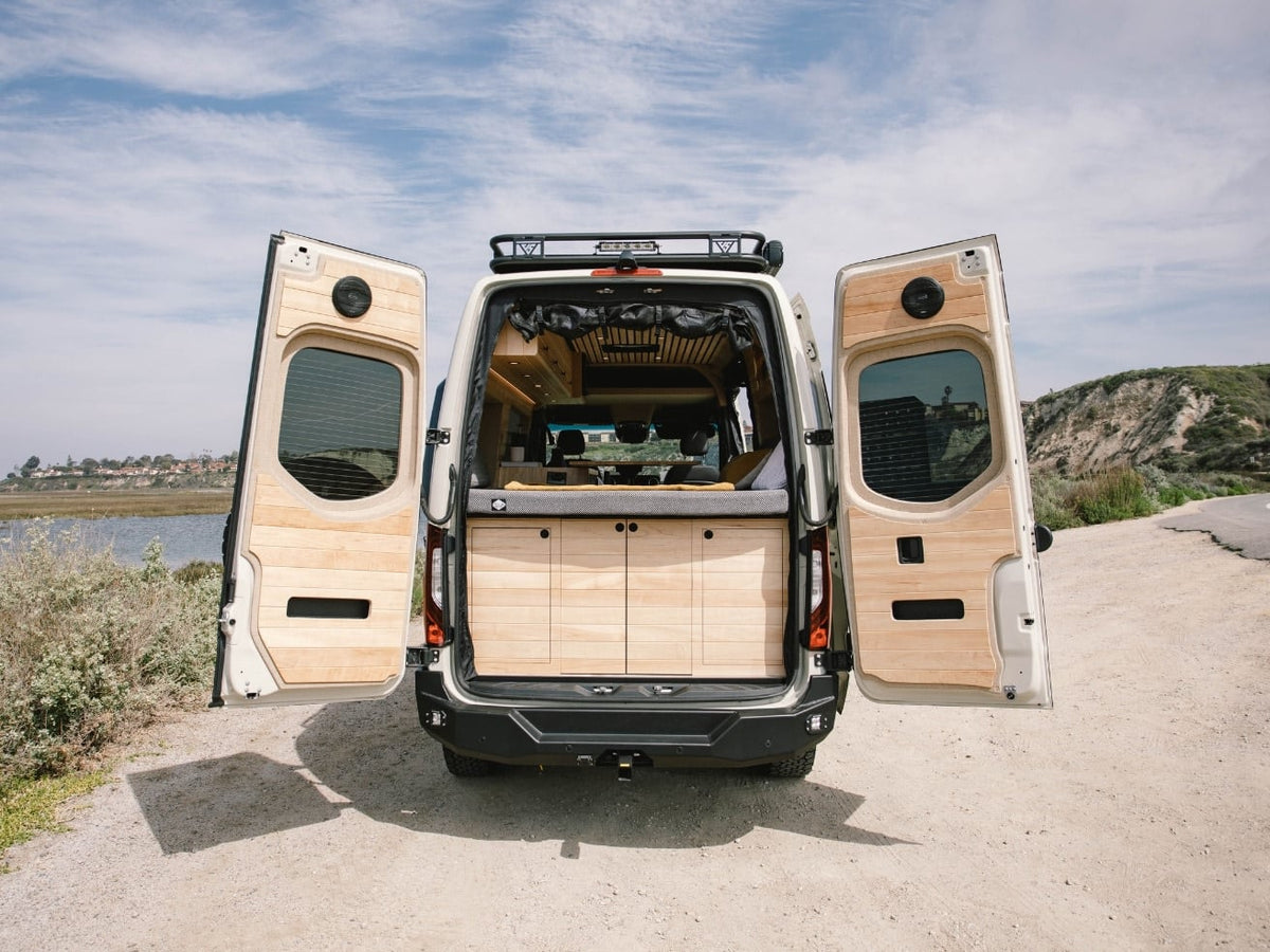  parked outdoors by water.|An RV rental's outdoor shower in action! A person holds the nozzle connected to the van — photo 16