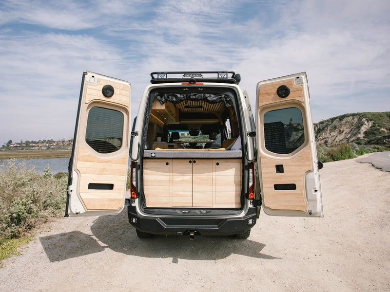  parked outdoors by water.|An RV rental's outdoor shower in action! A person holds the nozzle connected to the van — photo 16