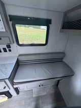 Cozy rv rental interior: a light grey bench dinette with striped backrest, window view of a field, and under-seat storage.