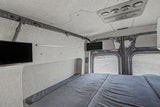 Inside an RV rental: a cozy bed, dual TVs, and custom fabric walls. Perfect for comfortable van life adventures.