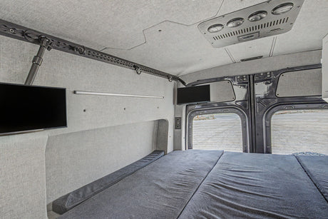 Inside an RV rental: a cozy bed, dual TVs, and custom fabric walls. Perfect for comfortable van life adventures.