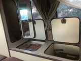 This RV rental interior features practical storage. Open compartments reveal space for books and gear, with a window view and mirror.