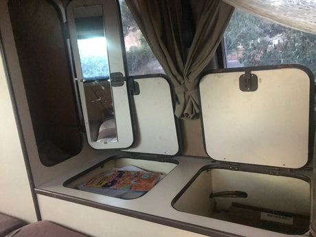This RV rental interior features practical storage. Open compartments reveal space for books and gear, with a window view and mirror.
