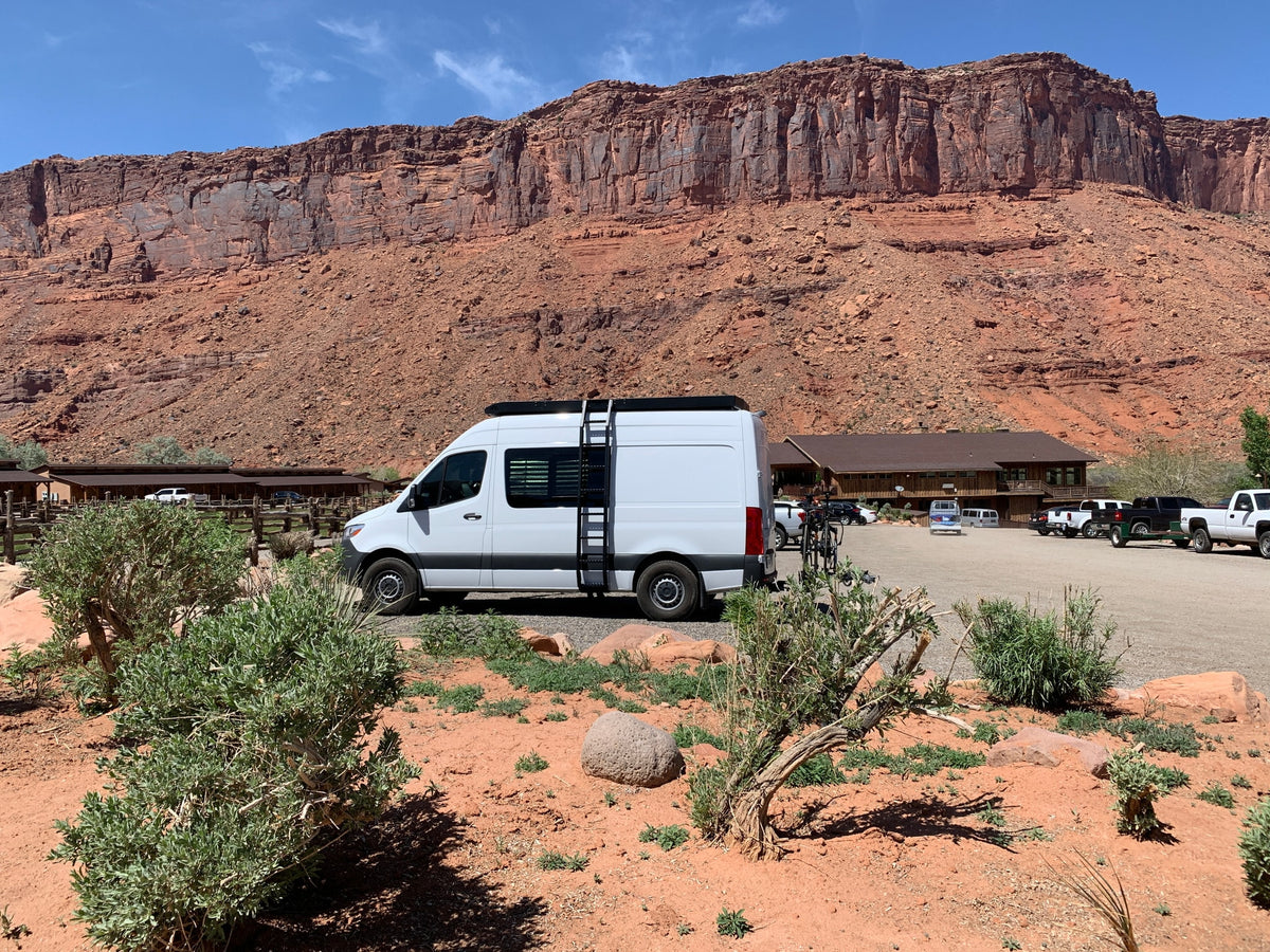 White RV rental at a desert lodge with majestic red rock cliffs and a blue sky in the background.