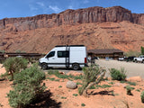 White RV rental at a desert lodge with majestic red rock cliffs and a blue sky in the background.