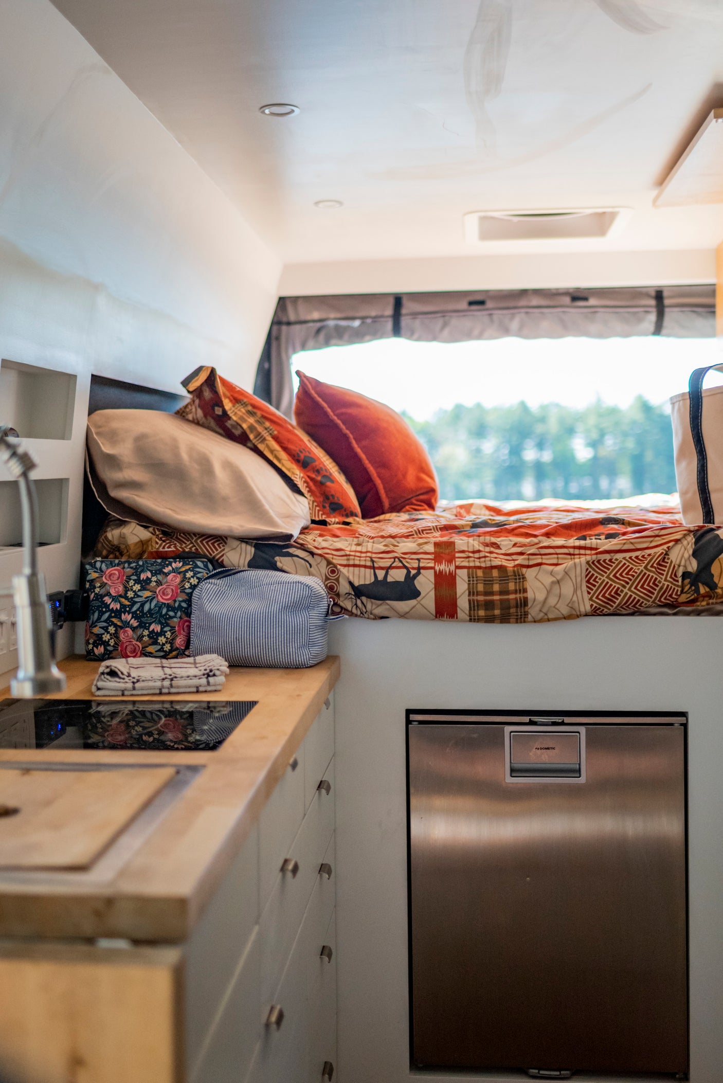 Compact RV rental: a bright interior with a comfy bed, kitchen, fridge, and scenic view.