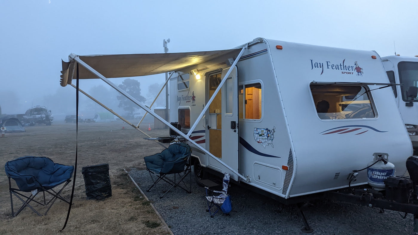 An RV rental, a Jay Feather travel trailer, set up with an awning and chairs in a misty morning campground. A crescent moon peeks through. — photo 15