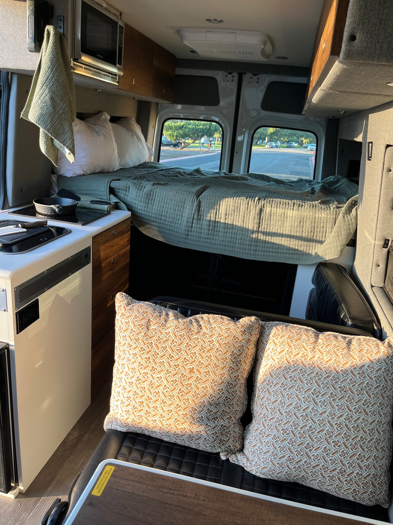 Inside an rv rental: comfortable bed, kitchen with microwave, and patterned pillows on a bench for a homey travel experience. — photo 29